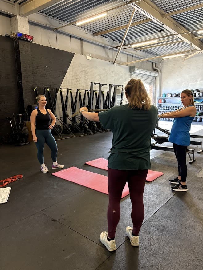 Kate standing and smiling while coaching two clients on mats