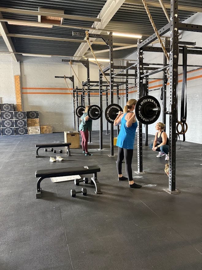 A client back-squatting a barbell while Kate watches from the rack